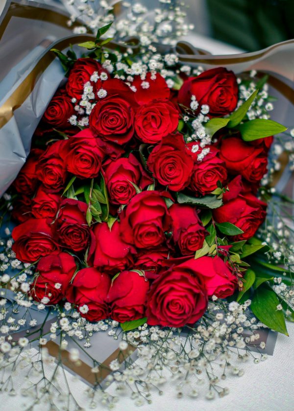 Stunning red rose bouquet with baby's breath on a white table, perfect for celebrations.